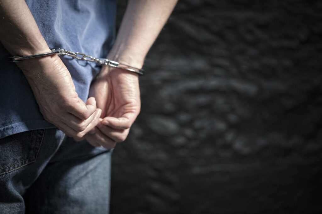 A man standing with his hands on his back on handcuffs, representing how one can benefit from calling a Portland criminal defense lawyer.