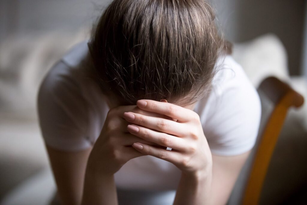 A woman lowering her face, covering her forehead with her hands, representing how one can benefit from calling a Maine criminal defense lawyer.