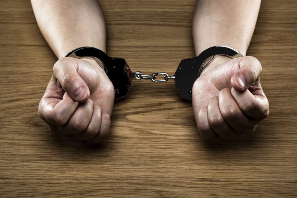 A man wearing handcuffs with his hands on a table, representing how one can benefit from calling a Maine criminal defense lawyer.