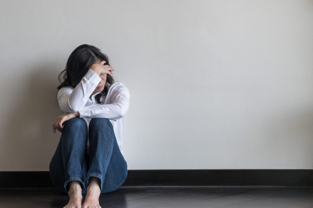 A woman sitting on the floor covering her face, representing how one can benefit from calling a Bangor Criminal Defense Attorney.