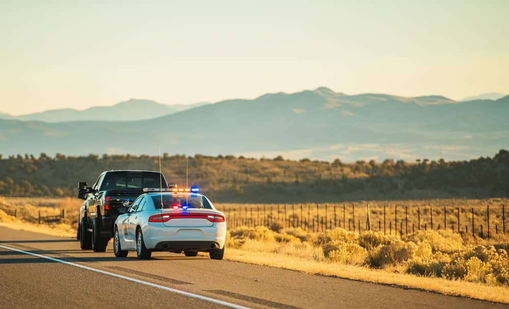 Driving without a license in Maine pictured by a police car pulling over a truck.