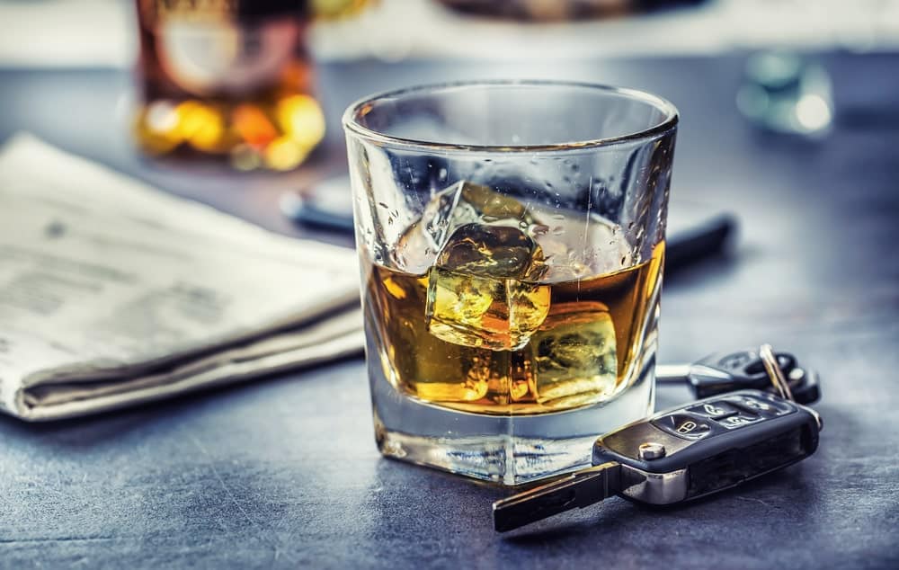 Top Ten OUI Mistakes in Maine portrayed by a glass of whiskey, car keys and a newspaper on a tabletop